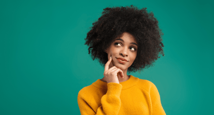 A young black woman with natural hair wears a yellow jumper and looks thoughtfully upwards