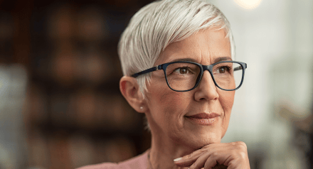 Middle aged white woman with short grey hair and glasses looking thoughtful